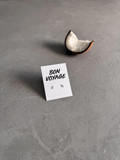 Sterling silver airplane earrings on a 'Bon Voyage' message card. The earrings are shown next to a segment of coconut. Sterling silver airplane earrings on a 'Bon Voyage' message card. The earrings are shown next to a segment of coconut.