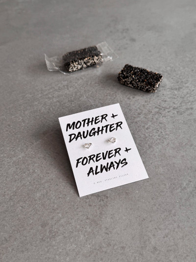 Sterling silver heart knot earrings on a 'Mother + Daughter' message card. The earrings are shown with black sesame candies. Sterling silver heart knot earrings on a 'Mother + Daughter' message card. The earrings are shown with black sesame candies.