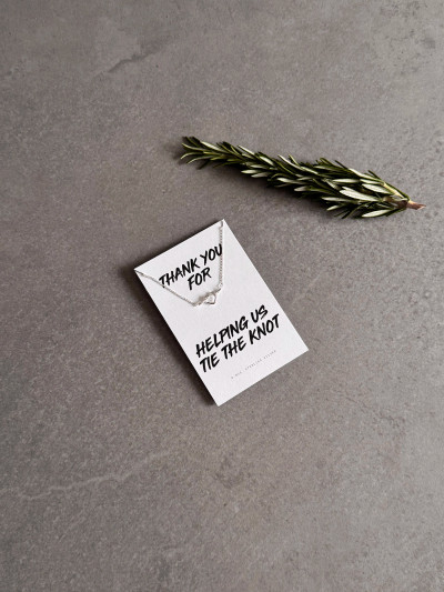 Sterling silver heart knot necklace on a 'Thank You For Helping Us Tie The Knot' message card. The necklace is shown next to a sprig of rosemary.