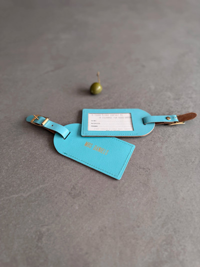 Handmade real leather luggage tags with gold coloured detailing and emboss. The luggage tags are shown in the turquoise option next to an olive.