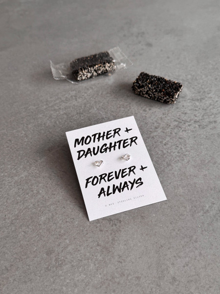 Sterling silver heart knot earrings on a 'Mother + Daughter' message card. The earrings are shown with black sesame candies.