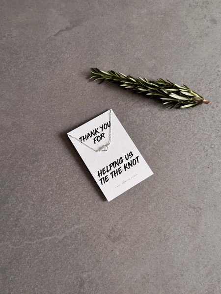 Sterling silver heart knot necklace on a 'Thank You For Helping Us Tie The Knot' message card. The necklace is shown next to a sprig of rosemary.