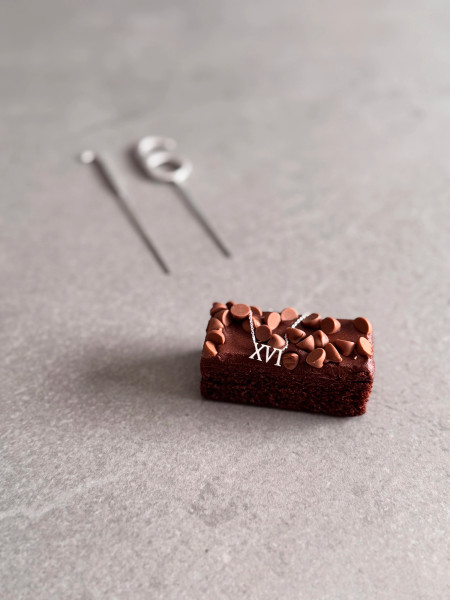 16th Birthday Gift Roman Numerals Necklace - Sterling Silver. The necklace is shown on a piece of cake with the number 16 sparklers in the background.