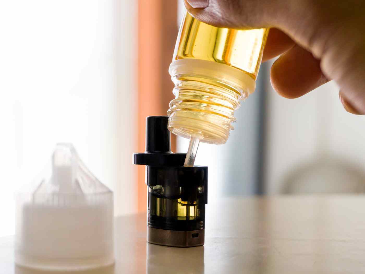 A hand pouring e-liquid from a shortfill bottle into a refillable pod, illustrating the formats affected by the October 2026 vaping tax.