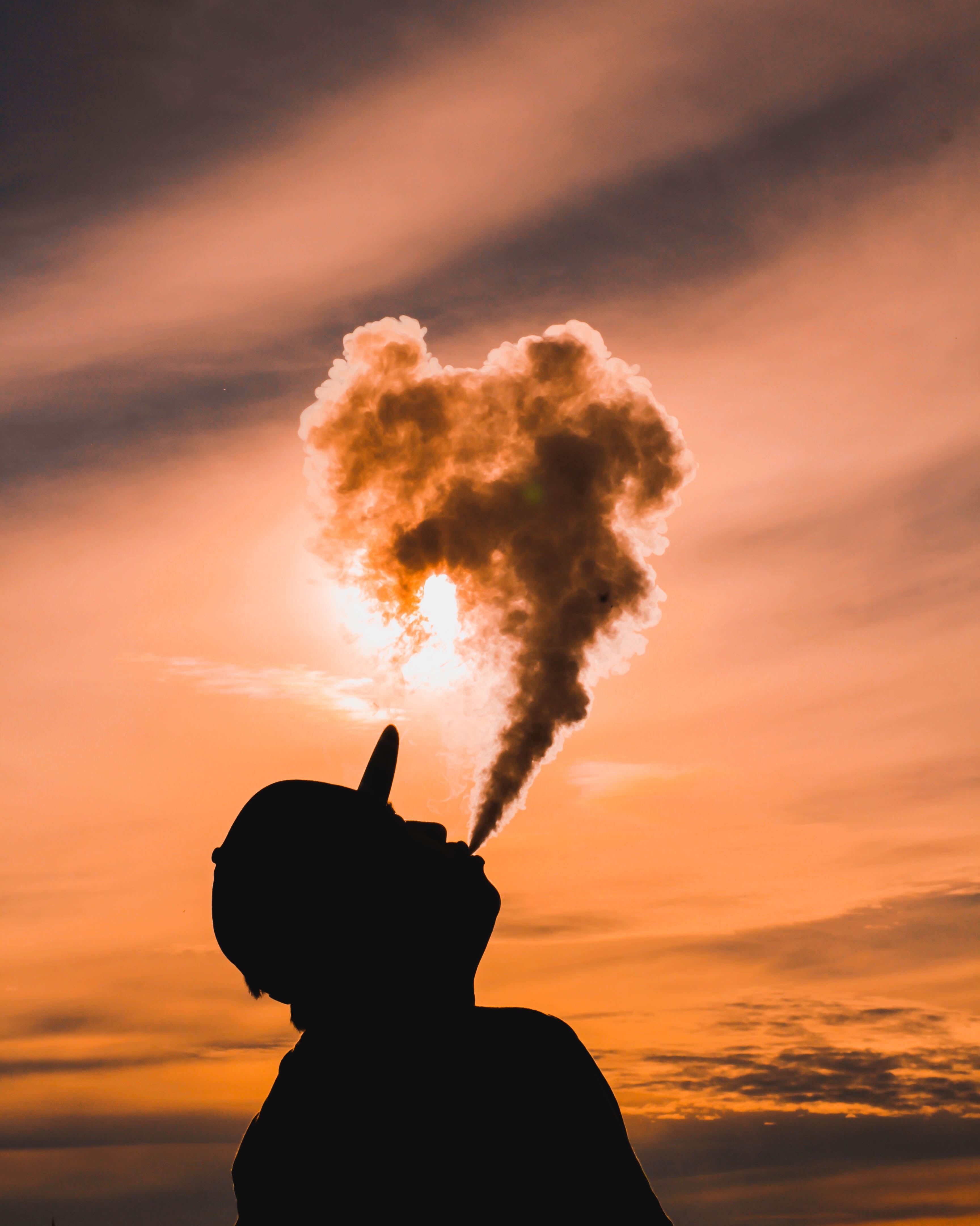 Man Puffing Large Clouds of Vapour With a Sunset Backdrop