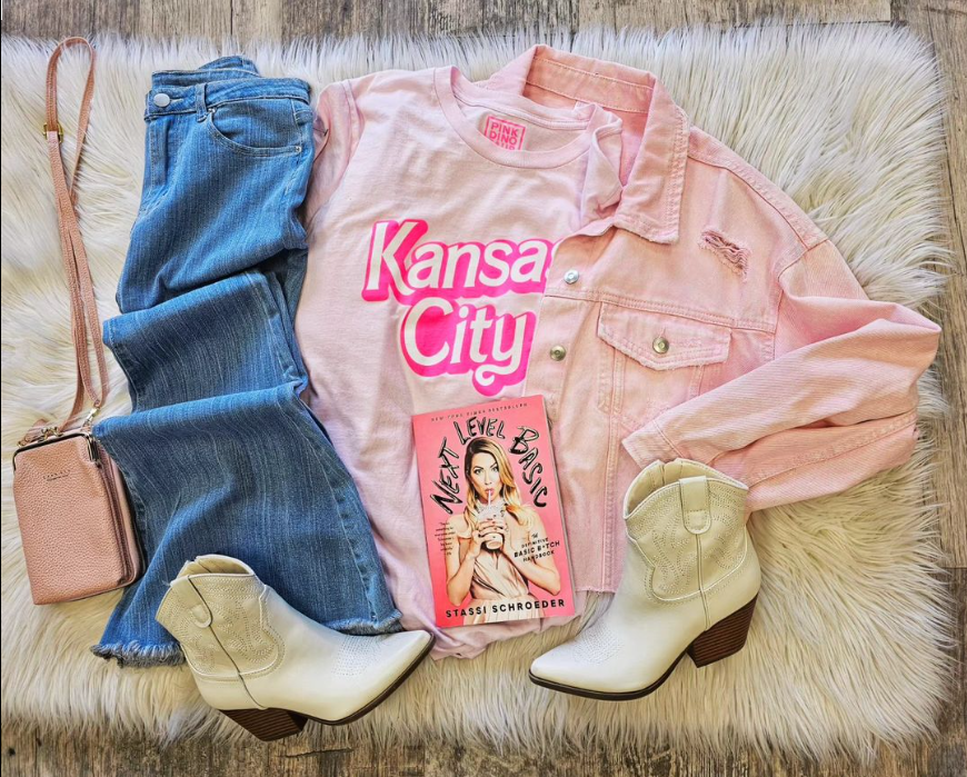 Trendy denim outfit with pink jacket featuring 'Kansas City' tshirt, cute boots and a book