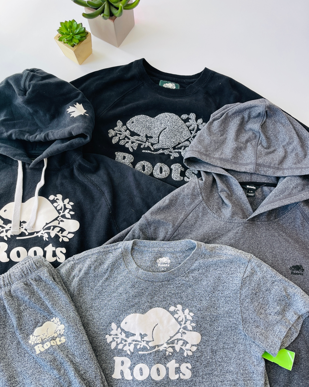 Roots brand sweatshirts and sweatpants laid out, main colours are grey.