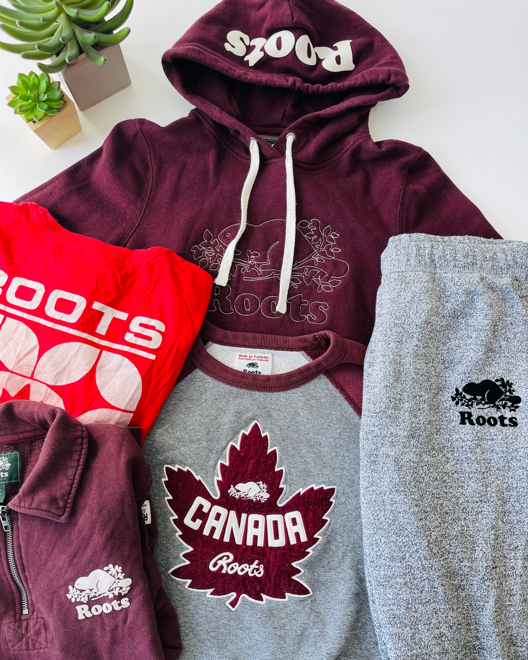 Roots brand sweatshirts and sweatpants laid out, main colours are red and grey.