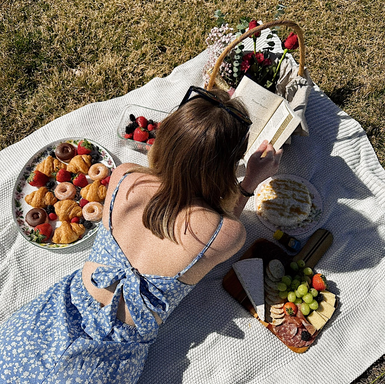 A girl in a blue dress laying on a picnic blanket reading a book