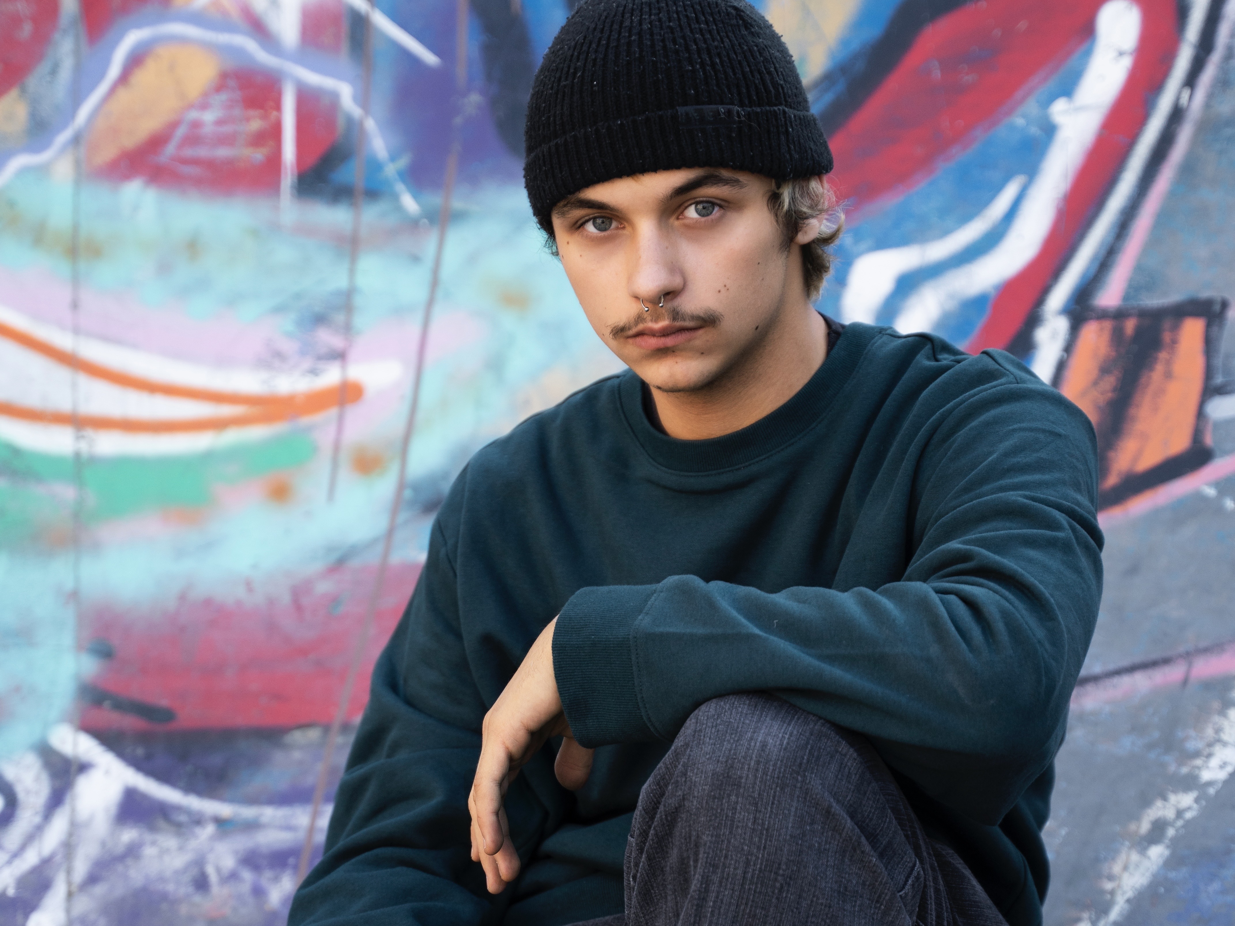 Young man wearing black beanie, green sweatshirt, and black jeans