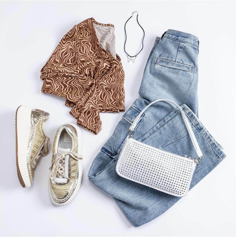 Gently used outfit spread out on white surface including a pair of blue jeans, a folded top, rhinestone purse,  necklace, and sneakers.