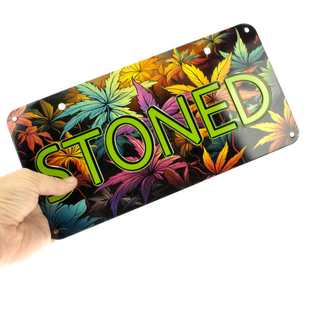 Hand holding a Stoned Embossed Metal License Plate with colorful cannabis leaf background and glossy finish