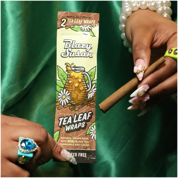 A woman holding a pack of Blazy Susan Tea Leaf Wraps with a rolled joint.