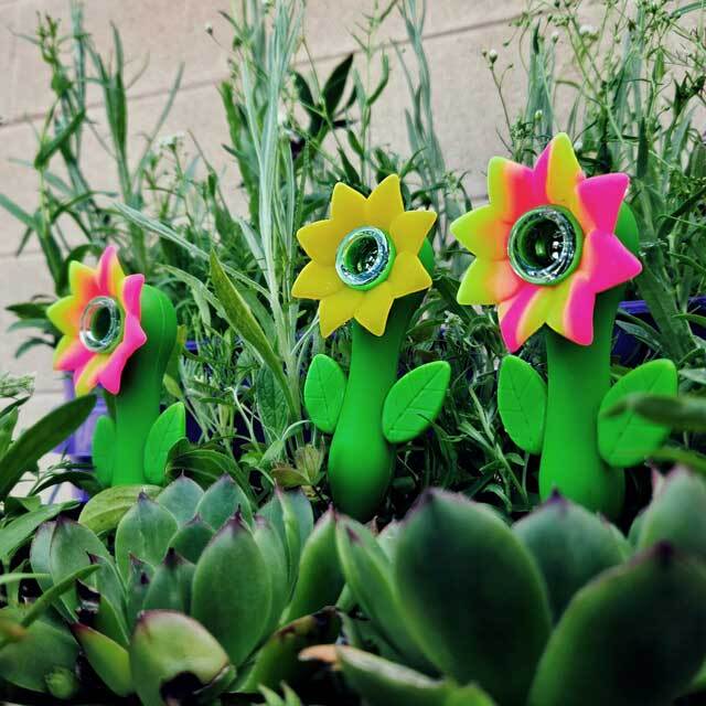 Three silicone sunflower hand pipes outside in the grass.