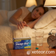 Close-up nightstand view of GoodSense Maximum Strength Nighttime Sleep-Aid (Diphenhydramine HCl 50mg) boxed product, water glass, alarm clock, and loose blue gelcap.