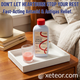A professional lifestyle marketing image for Foster & Thrive Maximum Strength Antacid & Antigas in cherry flavor. The blue product bottle sits on a white textured tray on a wooden bedside table next to a small glass filled with pink cherry-flavored liquid. In the soft-focus background are a bed and a desk lamp. The headline at the top reads 'DON’T LET HEARTBURN STOP YOUR REST' with the sub-headline 'Fast-Acting Antacid & Antigas Relief.' The xeteor.com logo is featured at the bottom.