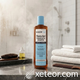 A bottle of Major Thera-Gel Therapeutic Shampoo resting on a wet grey marble countertop in a steamy, modern bathroom. The bottle is surrounded by spa-like elements, including neatly folded white towels, a wooden comb, a hairbrush, and a small glass bottle of oil, highlighting a relaxing hair care routine.