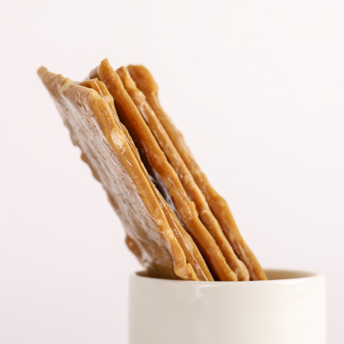 Pieces of golden MOA Stout Macadamia Brittle arranged upright in a white cup.