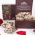 This image showcases an elegant arrangement of gourmet treats, featuring a box of "Dark Chocolate Macadamia & Cranberry Toffee Crunch" from Makana. The box, adorned with colourful heart motifs, hints at a special occasion or romantic gift. Inside, you can see the toffee crunch pieces, generously coated with dark chocolate and topped with crushed nuts and cranberries.

Surrounding the box are vibrant red roses, adding a touch of romance, while scattered rose petals enhance the overall romantic and indulgent atmosphere. The clean, white background makes the colours pop, drawing attention to both the luxurious chocolate treat and the beautiful flowers, creating an inviting presentation perfect for gifting or celebrating special moments.