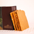 Pieces of golden MOA Stout Macadamia Brittle arranged upright against a luxurious brown Makana Confections branded gift box.