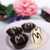 The picture features a delightful arrangement of elegantly crafted chocolates on a soft pink plate, surrounded by colourful floral elements, creating a whimsical and inviting atmosphere.

In detail, the image showcases four chocolates: two are dark chocolate with decorative white chocolate drizzles and presented in petite black paper cups, while the other two are white chocolate, also adorned with rich dark chocolate lines. The plate is a gentle pink hue, enhancing the visual appeal of the sweets. In the background, soft-focus flowers in shades of pink and purple suggest a floral arrangement, contributing to a charming, celebratory mood. The overall feel of the image is warm and inviting, perfect for a springtime treat or a special occasion.