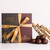 Makana Confections arrangement of handmade Bourbon Truffles and Dark Chocolate Macadamia Butter Toffee Crunch besides a ribboned branded gift box.