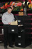Phoenix LTR4W31 4-drawer fireproof file cabinet in black - office scene with open drawer and man filing letter-size folders