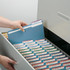 Hand placing a blue 1/3-cut tab file folder into a labeled filing cabinet drawer