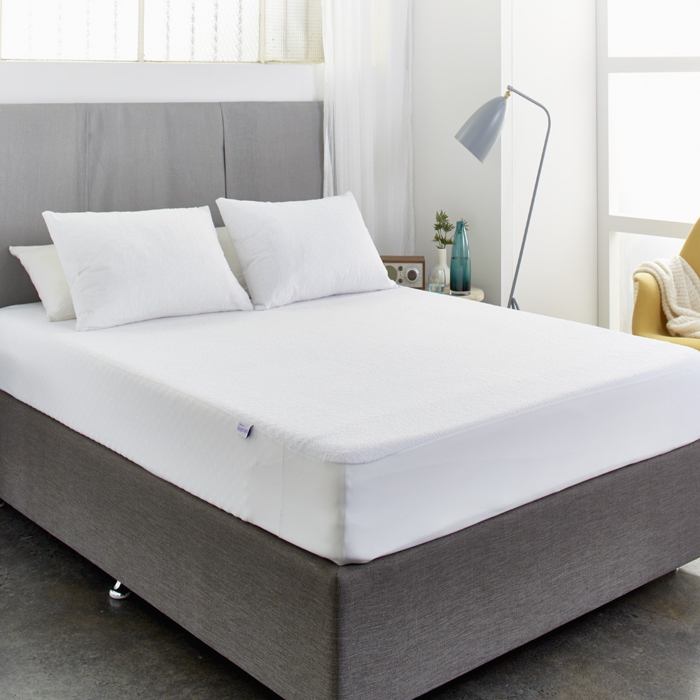 A fitted cotton terry waterproof mattress protector on a styled bed