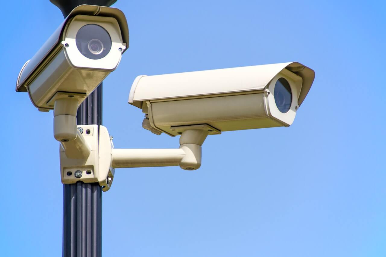 white CCTV camera mounted on black post under clear blue sky