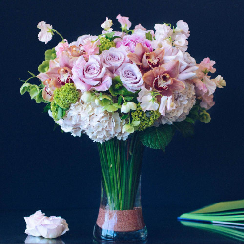 Lush and whimsical, this blush bouquet is sure to take your breath away. Blush peonies, peach cymbidium blooms, and blush roses rest atop clouds of hydrangea while softly hued sweet peas and bunches of vibernum sprout out from all angles. This stunning design rests within a 12" tall flared cylinder glass vase complete with metallic rose gold sand, and stands at approximately 20" tall and 17" wide overall. **Please note that peonies are currently out of season and a substitute will be used in their place** Lush and whimsical, this blush bouquet is sure to take your breath away. Blush peonies, peach cymbidium blooms, and blush roses rest atop clouds of hydrangea while softly hued sweet peas and bunches of vibernum sprout out from all angles. This stunning design rests within a 12" tall flared cylinder glass vase complete with metallic rose gold sand, and stands at approximately 20" tall and 17" wide overall. **Please note that peonies are currently out of season and a substitute will be used in their place**
