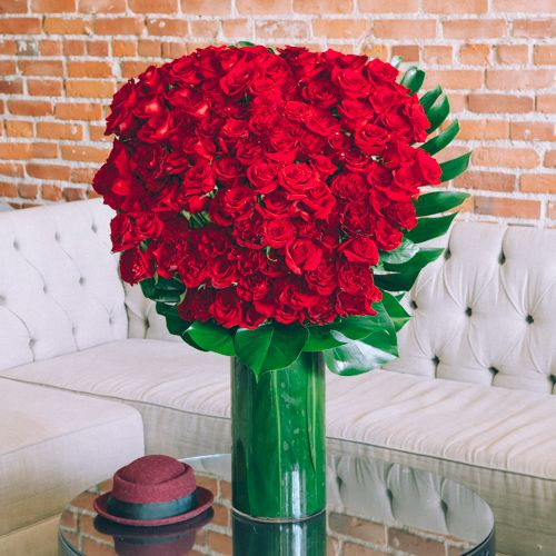 What’s in a name? This beautiful floral design holds the answer at its core. ONE HUNDRED perfect red roses bloom towards you, as monstera leaves accent behind the blooms. Monstera also lines the interior of the 22” by 9” cylindrical glass vase. Overall, this lush arrangement stands 37” tall and 28” wide, standing as a statement itself. What’s in a name? This beautiful floral design holds the answer at its core. ONE HUNDRED perfect red roses bloom towards you, as monstera leaves accent behind the blooms. Monstera also lines the interior of the 22” by 9” cylindrical glass vase. Overall, this lush arrangement stands 37” tall and 28” wide, standing as a statement itself.