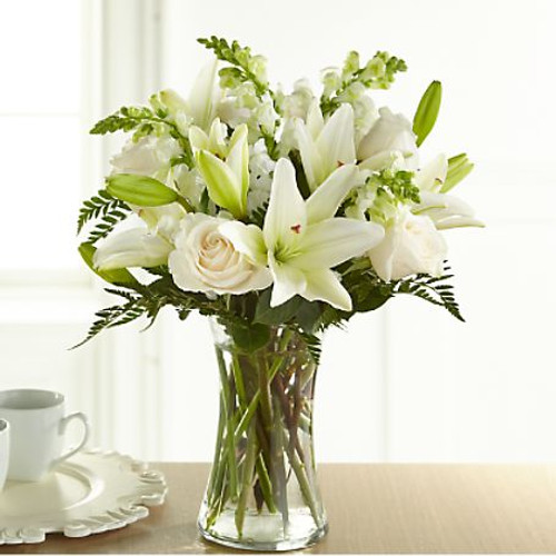 An exuberance of bright and beautiful white blossoms provides an exquisite way to deliver your expressions of sympathy and comfort. This life affirming tribute combines white roses, snapdragons and Asiatic lilies accented by lush greens arranged in a clear glass 8" vase. An excellent choice for a wake, funeral service or for sending your condolences to the home of grieving family or friends.