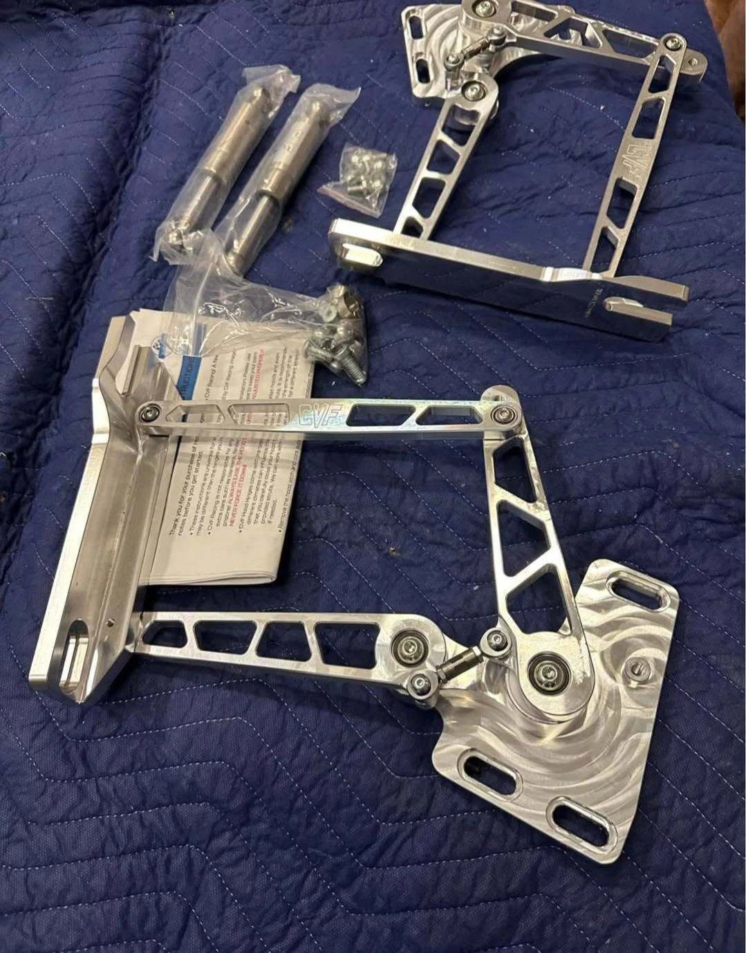 A pair of CVF billet hood hinges laid out with gas struts, hardware and instruction sheet