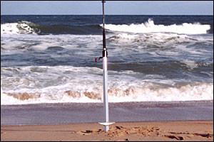 ANGLER'S FISH-N-MATE Fish-N-Mate 266 Sand Spike Anodized, a sturdy beach fishing sand spike standing on the sandy shore with the ocean in the background.