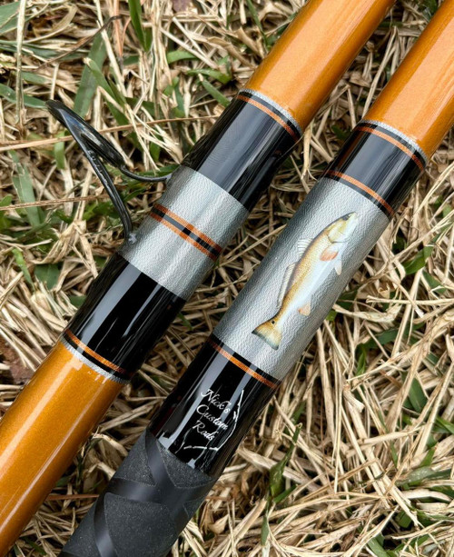 Nick's Custom Rods 2025, CTS 1305 fishing rod with a detailed fish illustration and black and orange accents, lying on grass.