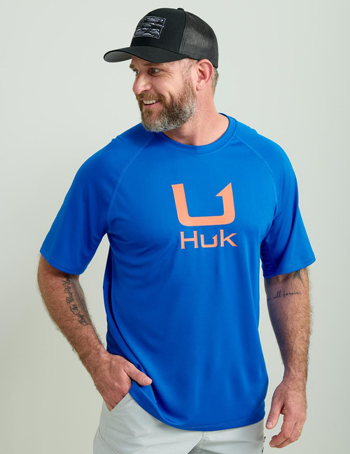 HUK Icon SS Crew, a man wearing a blue athletic t-shirt with the HUK logo in orange.