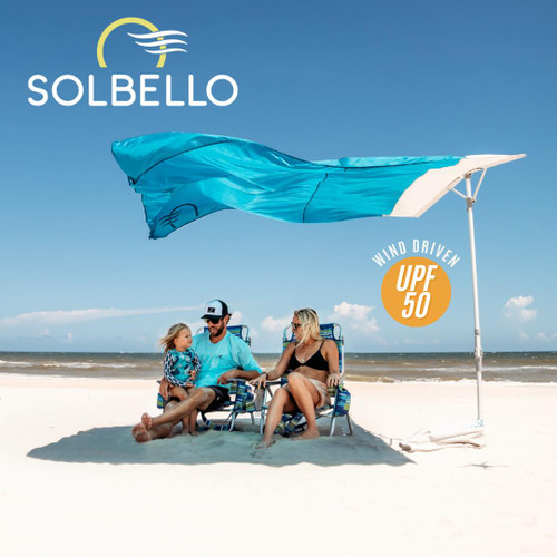 Solbello Sun Shade, a portable beach sunshade with wind-driven UPF 50 protection, blue fabric, and a white pole on a sandy beach under a clear sky.