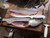 DEXTER RUSSELL Dexter SG133-7-WS SofGrip 7" Narrow Fillet Knife, With Sheath, white-handled fillet knife displayed beside a fish being cleaned on a wooden cutting board.
