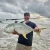NINJA TACKLE Ninja Tackle 7' Dagger Spinning Rod, man holding a large fish on the beach during cloudy weather.