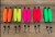 Four Horsemen Skinny Corks, colorful fishing lures with orange, yellow, pink, red, and green bodies with black tips and metal clips on a wooden surface.