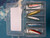 SHORELURE Shore Lure Sting Silver Tackle Box - 2 oz., empty tackle box with five fishing lures inside, including white, gold, pink, blue, and red-colored lures, organized in separate compartments.