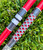 Nick's Custom Rods 2025, CTS 1305 fishing rod with a vibrant geometric patterned grip and a red shaft, lying on green grass.
