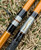 Nick's Custom Rods 2025, fishing rod with custom fish design and graphite grip, on grass background.