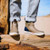 XTRATUF Xtratuf XMABV300 Ankle Deck Boot, close-up of tan waterproof ankle boots worn by person standing on a wooden surface outdoors with jeans rolled up.