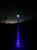 Reel Glo Sand Spike Reel Illuminator, illuminated sand spike with LED lights glowing in blue and green in a dark outdoor setting.