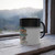 PRINTIFY F&F Sign Post Color Morphing Mug, 11oz, white and black ceramic mug with a black handle and color morphing feature, placed on a wooden windowsill with mountain view background.