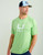 HUK Icon SS Crew, light green athletic T-shirt worn by a male model with a blue and white trucker cap.
