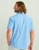 HUK Kona Solid SS, a light blue men's short-sleeve shirt, shown from behind on a male model with long wavy hair, standing against a plain background.