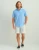 HUK Kona Solid SS, man wearing light blue short-sleeve button-up shirt with chest pocket, beige shorts, and slip-on shoes.